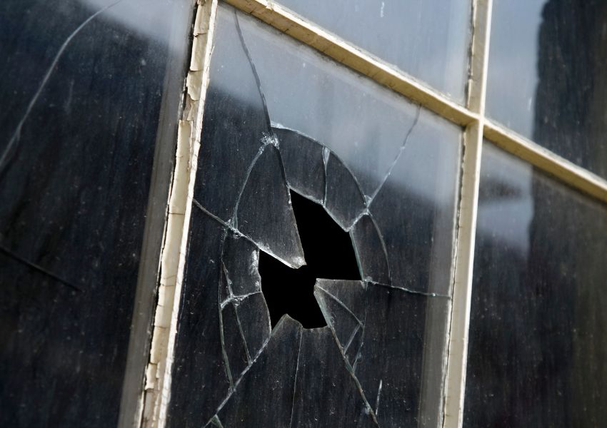 A close up of a broken window pane is featured, shattered in the center of the frame.